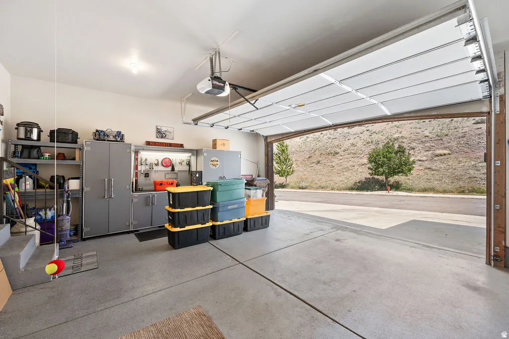 Two-car garage featuring a concrete floor, automatic overhead door, built-in cabinetry, and shelving units