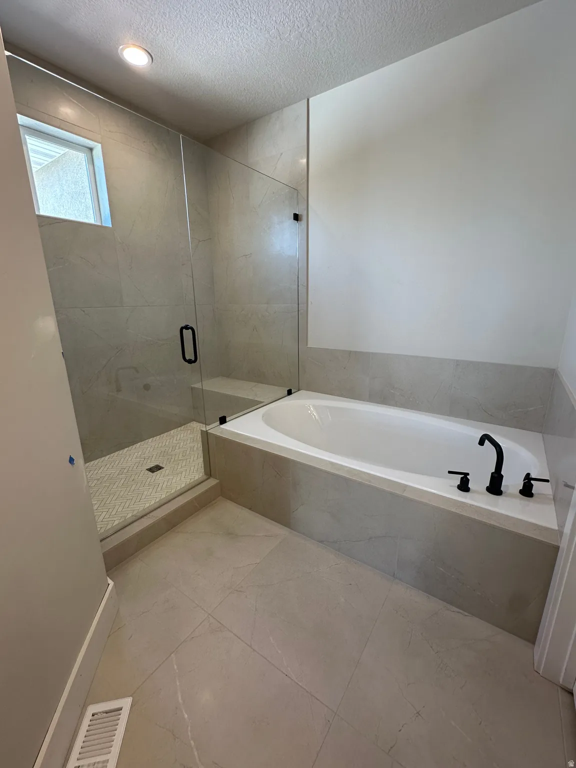 Spacious bathroom featuring a built-in soaking tub, a walk-in shower with a glass enclosure, large format floor tiling, a tiled shower surround, and matte black fixtures