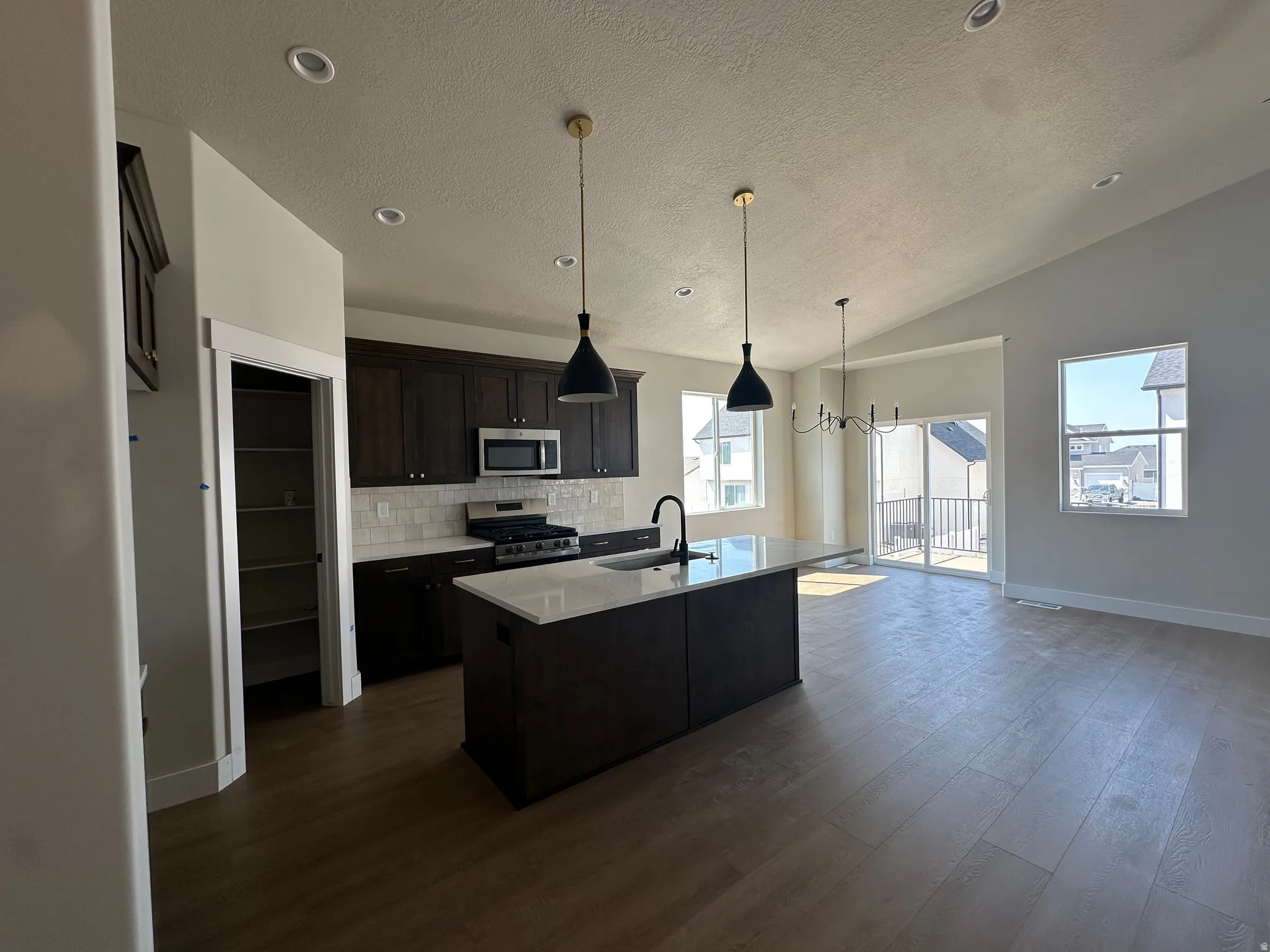 Open-concept kitchen with wood-finish flooring, dark wood cabinetry, white subway tile backsplash, and recessed lighting