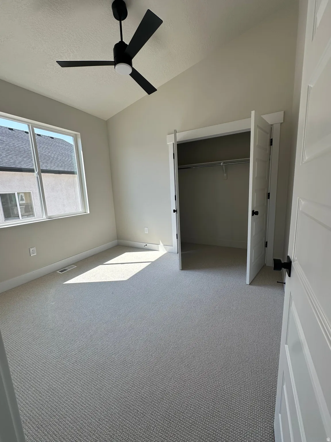 Neutral-toned carpeting with white trim, a modern black ceiling fan, and a double-door closet with black hardware