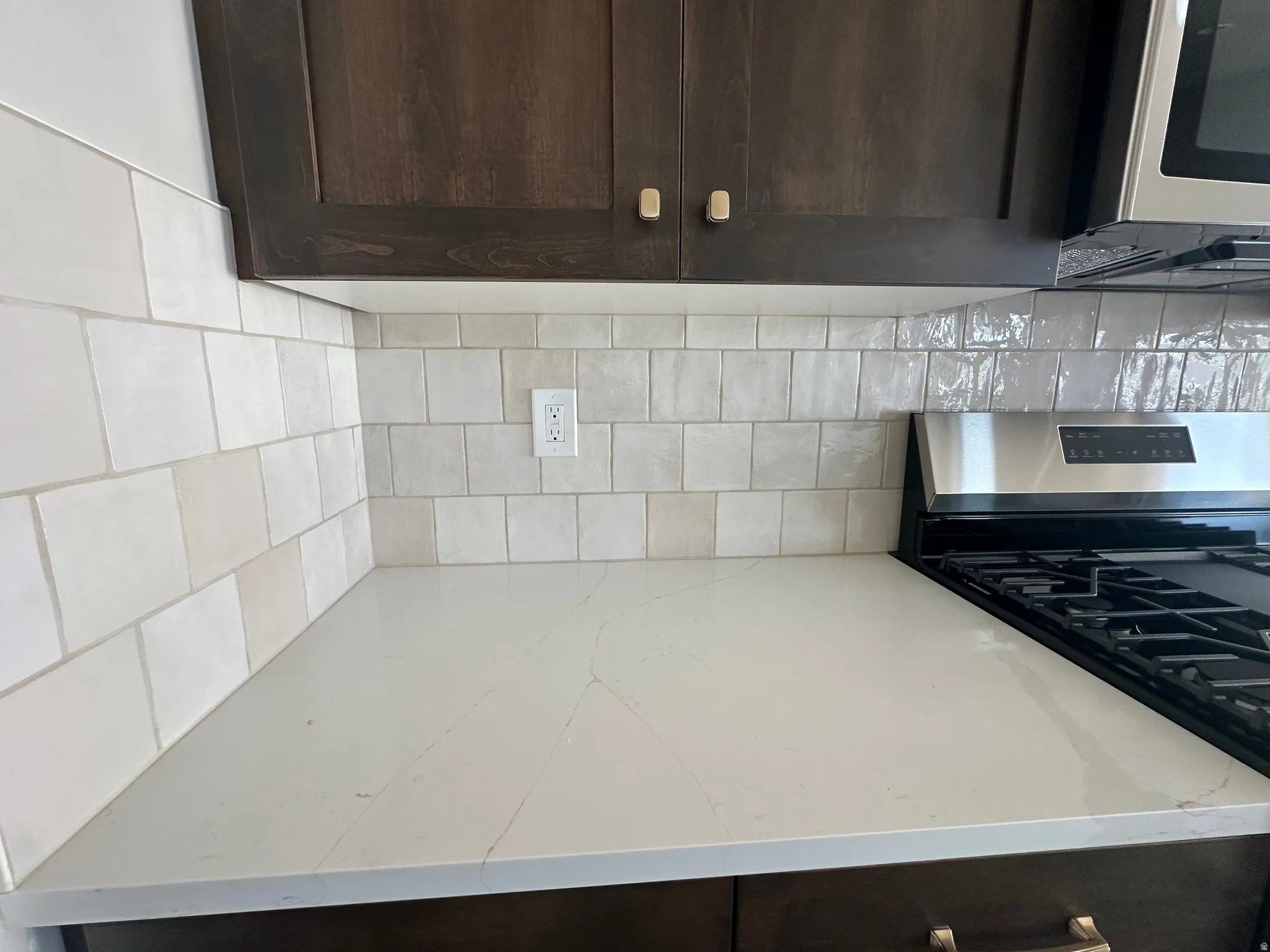 Quartz countertop, subway tile backsplash, dark wood cabinetry, stainless steel range, and built-in microwave