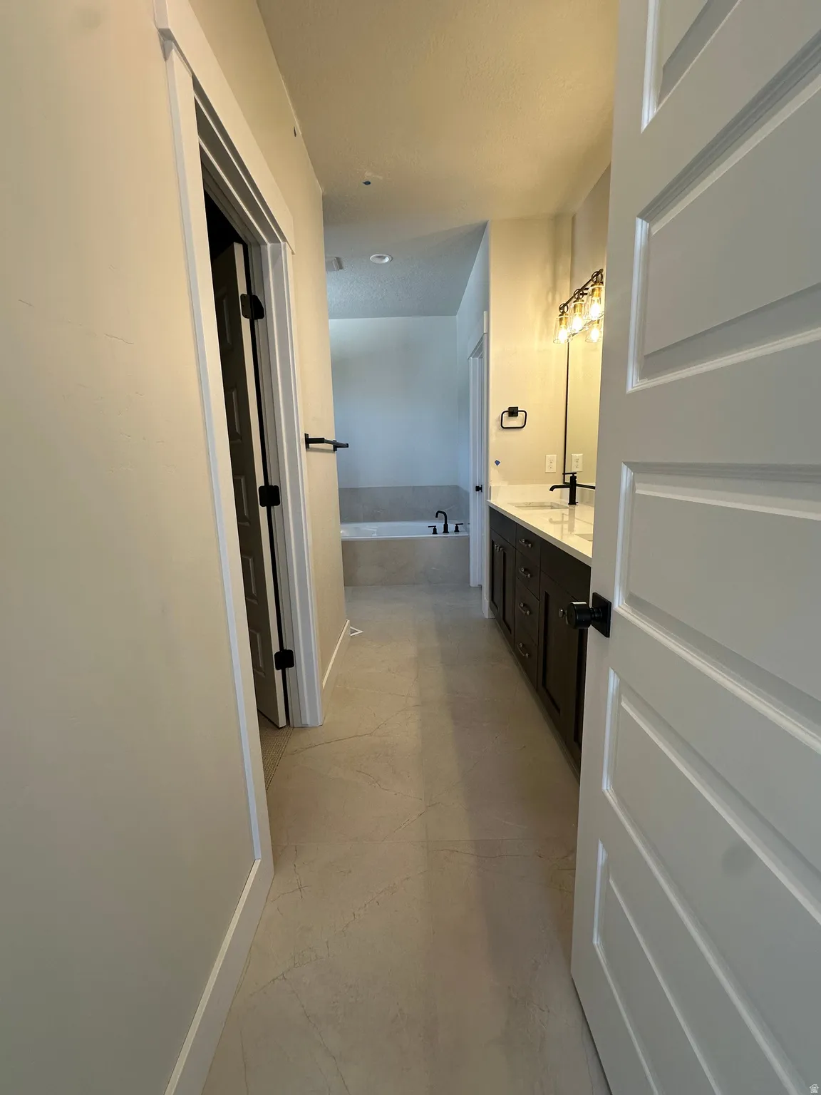 Hallway bathroom featuring a double vanity, dark wood cabinetry, white countertops, built-in bathtub, and tile flooring