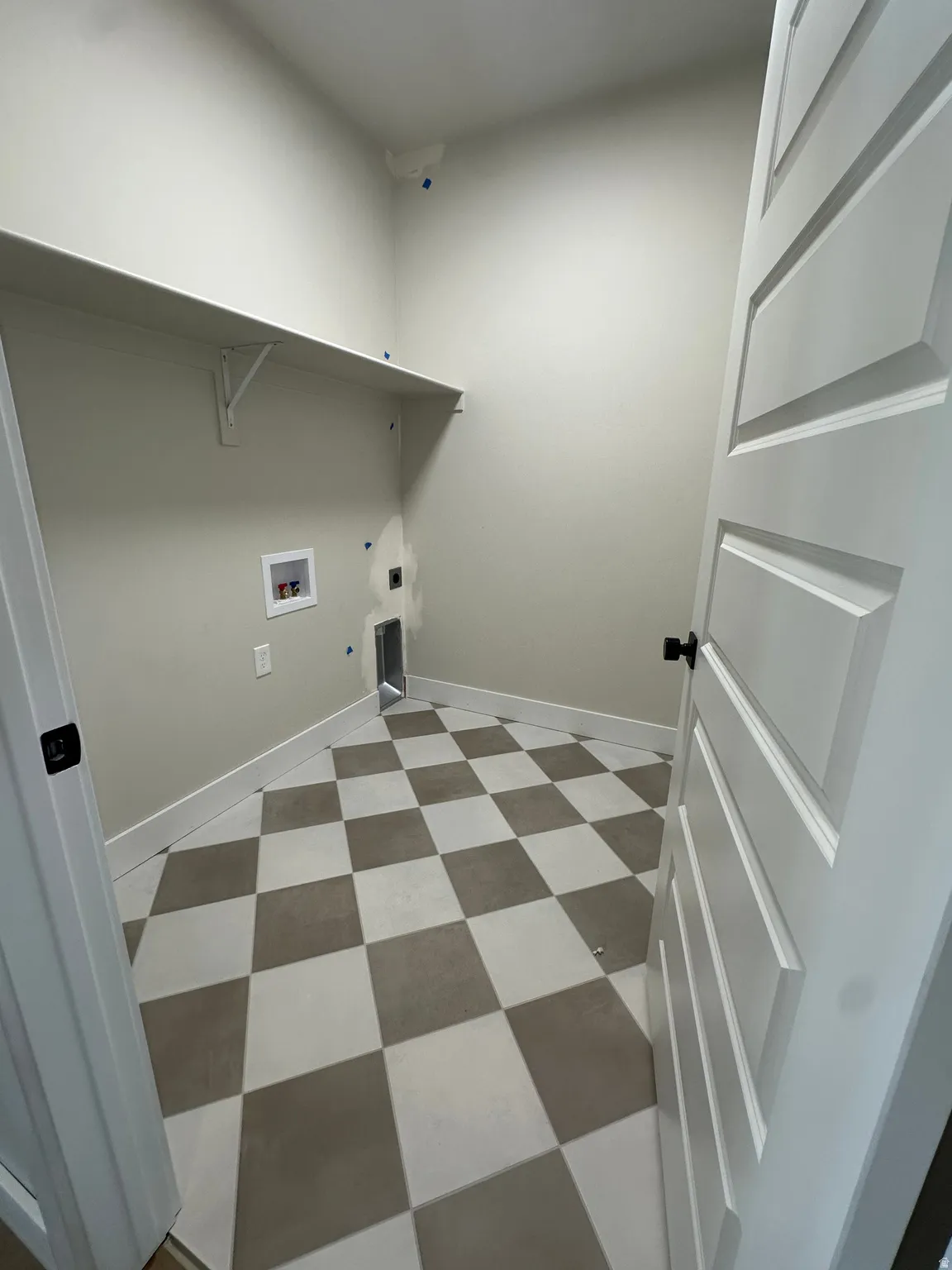 Checkered floor tiling, built-in shelving, white paneled door, and neutral wall tones
