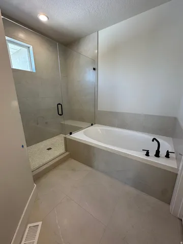 Spacious bathroom featuring a built-in soaking tub, a walk-in shower with a glass enclosure, large format floor tiling, a tiled shower surround, and matte black fixtures
