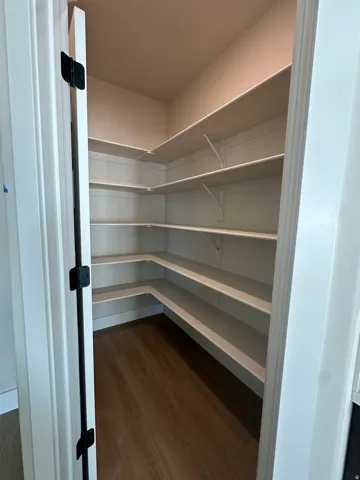 Walk-in pantry featuring extensive built-in shelving, wood-finish flooring, and white trim