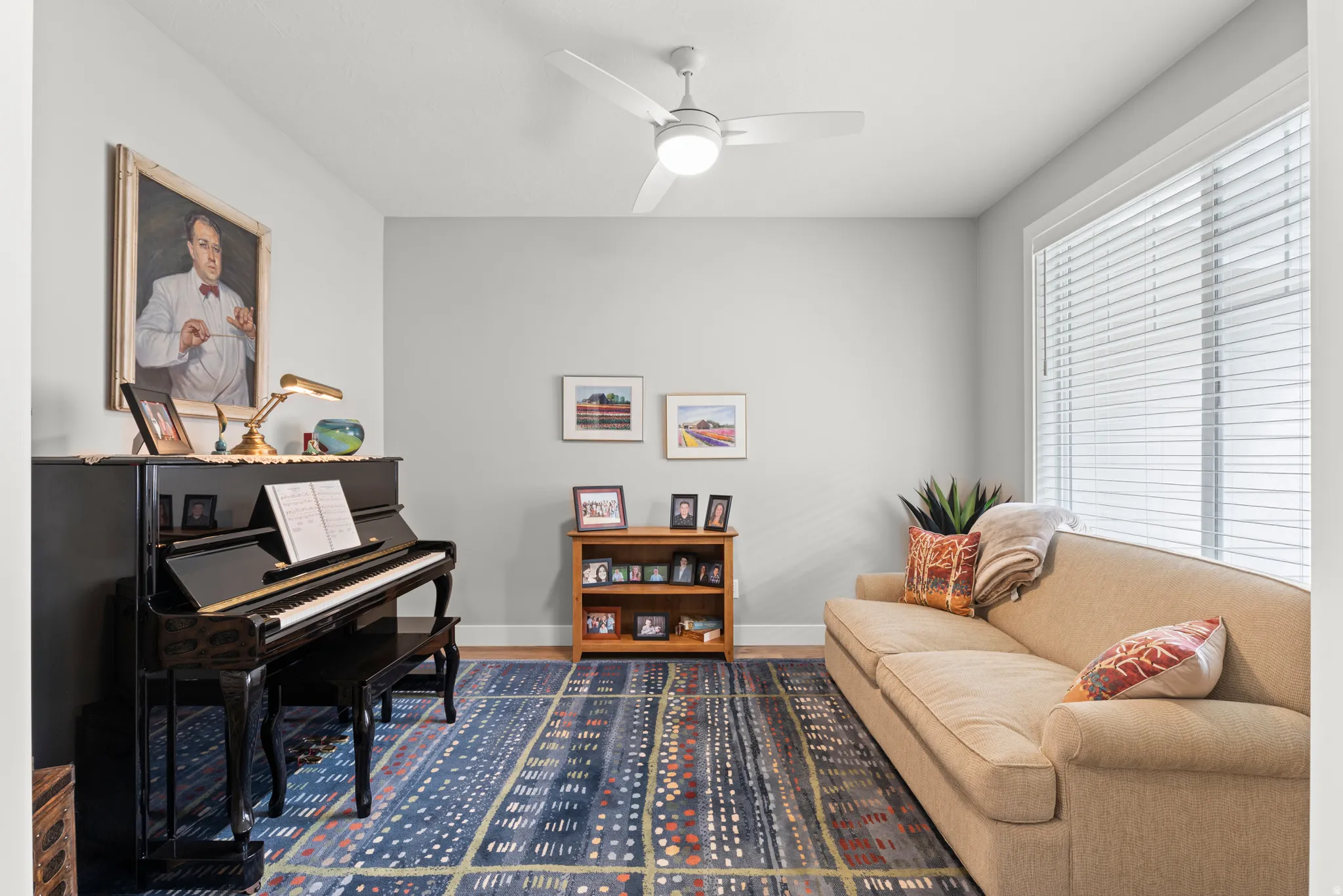 Neutral wall color, overhead ceiling fan with light fixture, large window with blinds, wood-finish baseboards, and wood-finish flooring