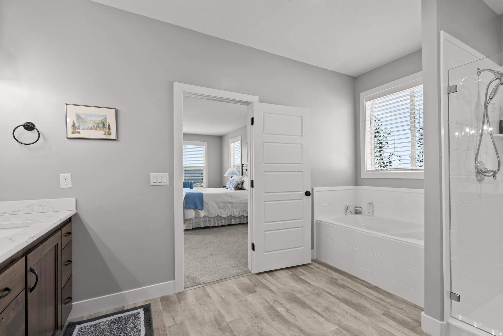 Bathroom featuring a built-in soaking tub, glass-enclosed shower, wood-finish flooring, and a vanity with a white countertop