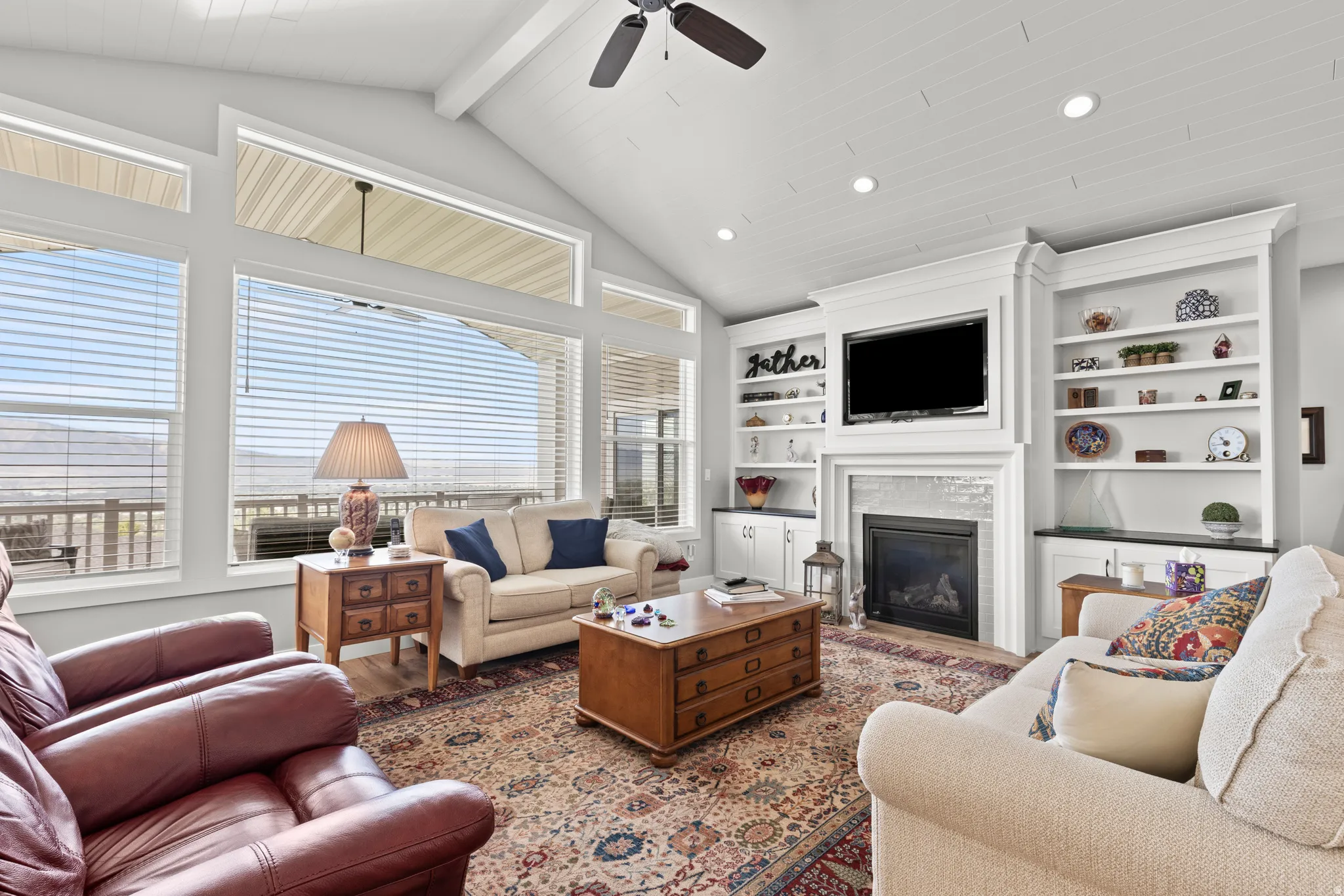 Vaulted ceiling with exposed beams, built-in shelving, integrated fireplace, wall-mounted television, and large windows