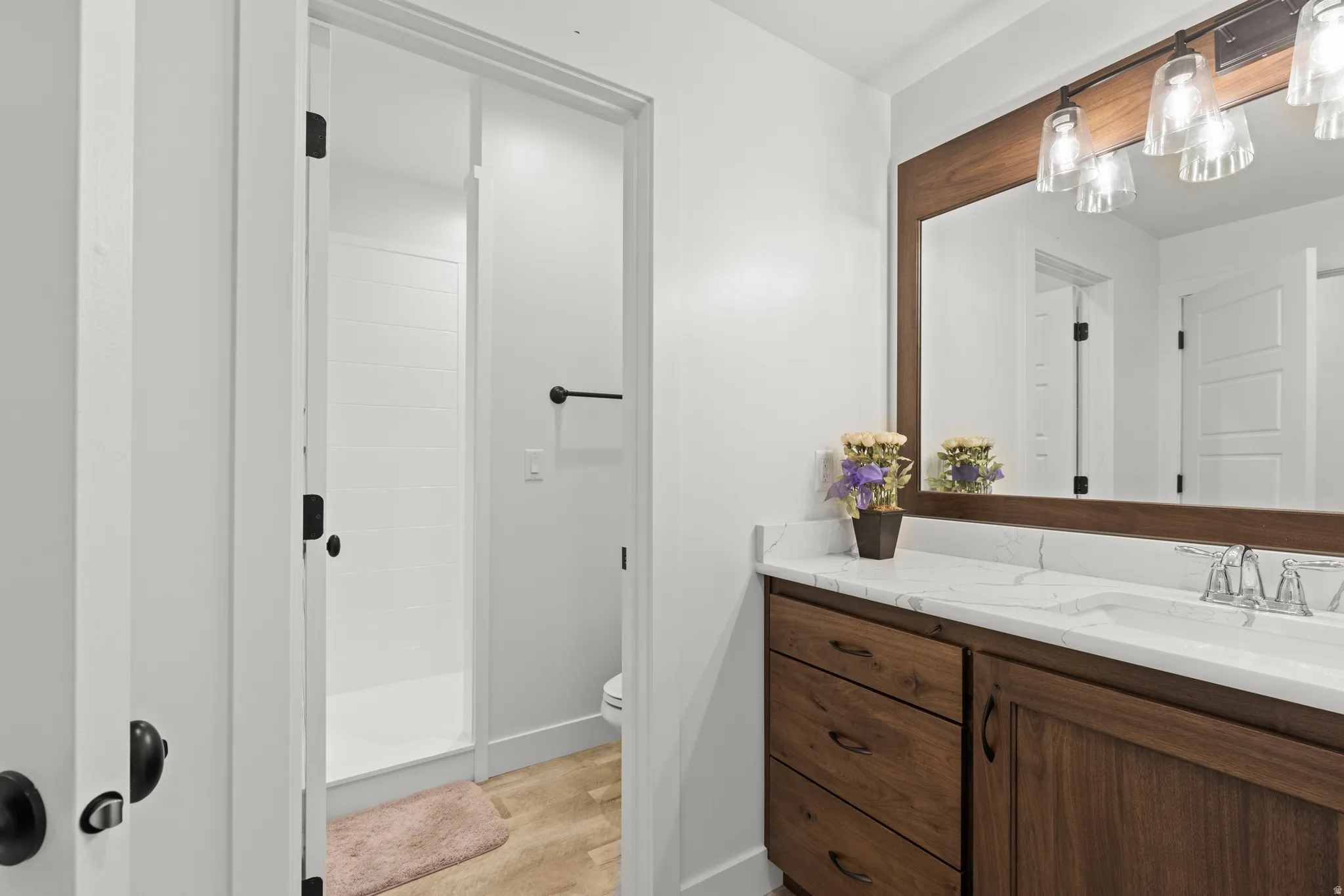 Bathroom vanity featuring a wood-finish frame mirror with clear glass sconce lighting, a single undermount sink, and a stone countertop