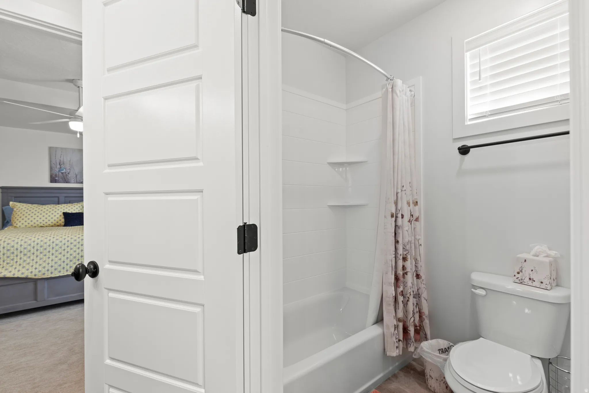Full bathroom featuring a white tub/shower combination with integrated shelving, a toilet, and a window with blinds