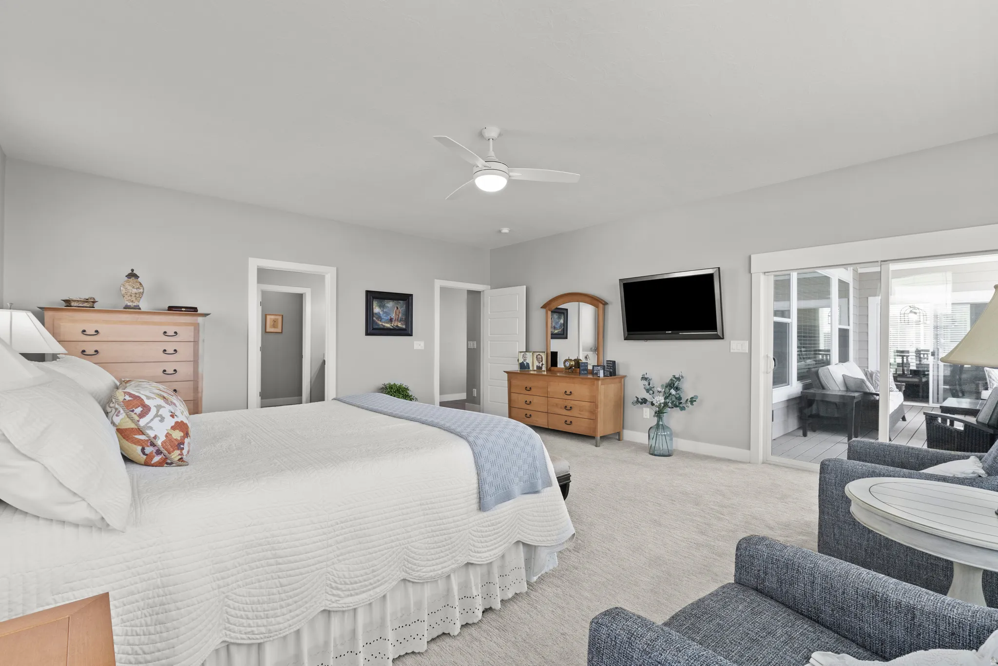 Spacious bedroom featuring light-toned carpeting, neutral wall paint, a ceiling fan, and access to an enclosed outdoor area through sliding glass doors