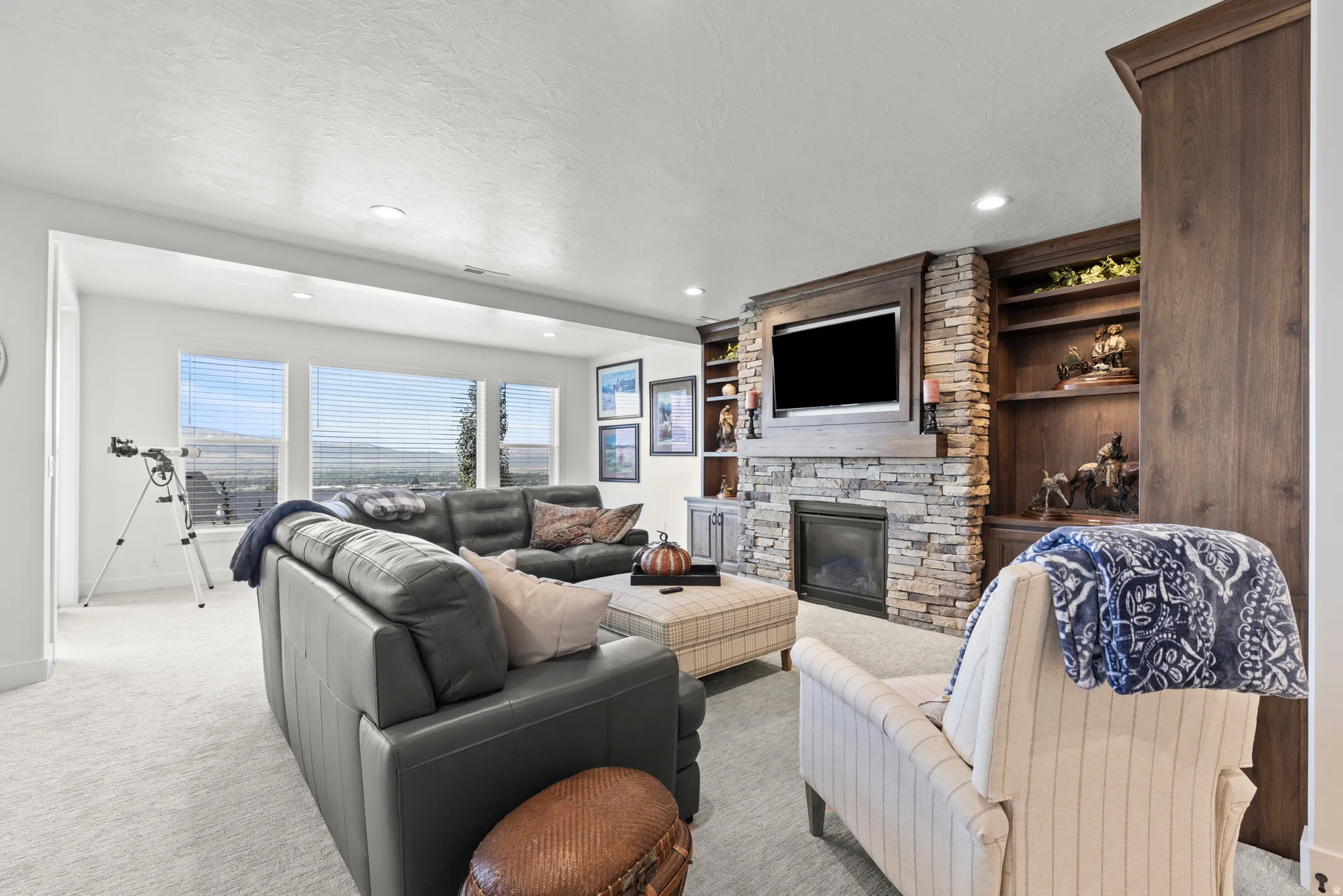Living area featuring a stacked stone fireplace with an integrated media center, built-in shelving, recessed lighting, and multiple windows