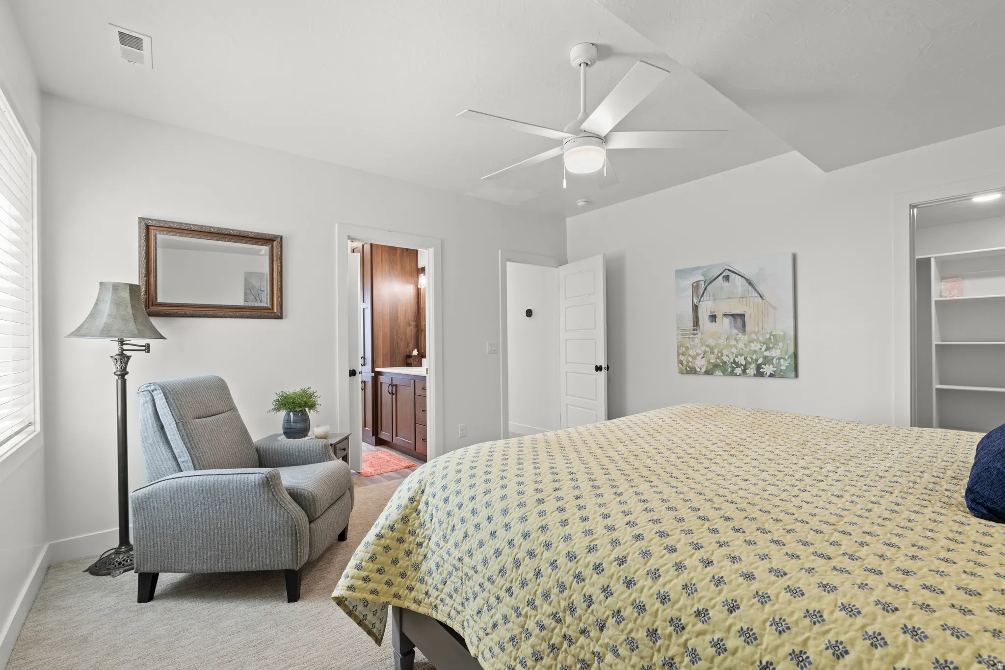 Bright bedroom with light-colored carpeting, a ceiling fan, and a window with blinds