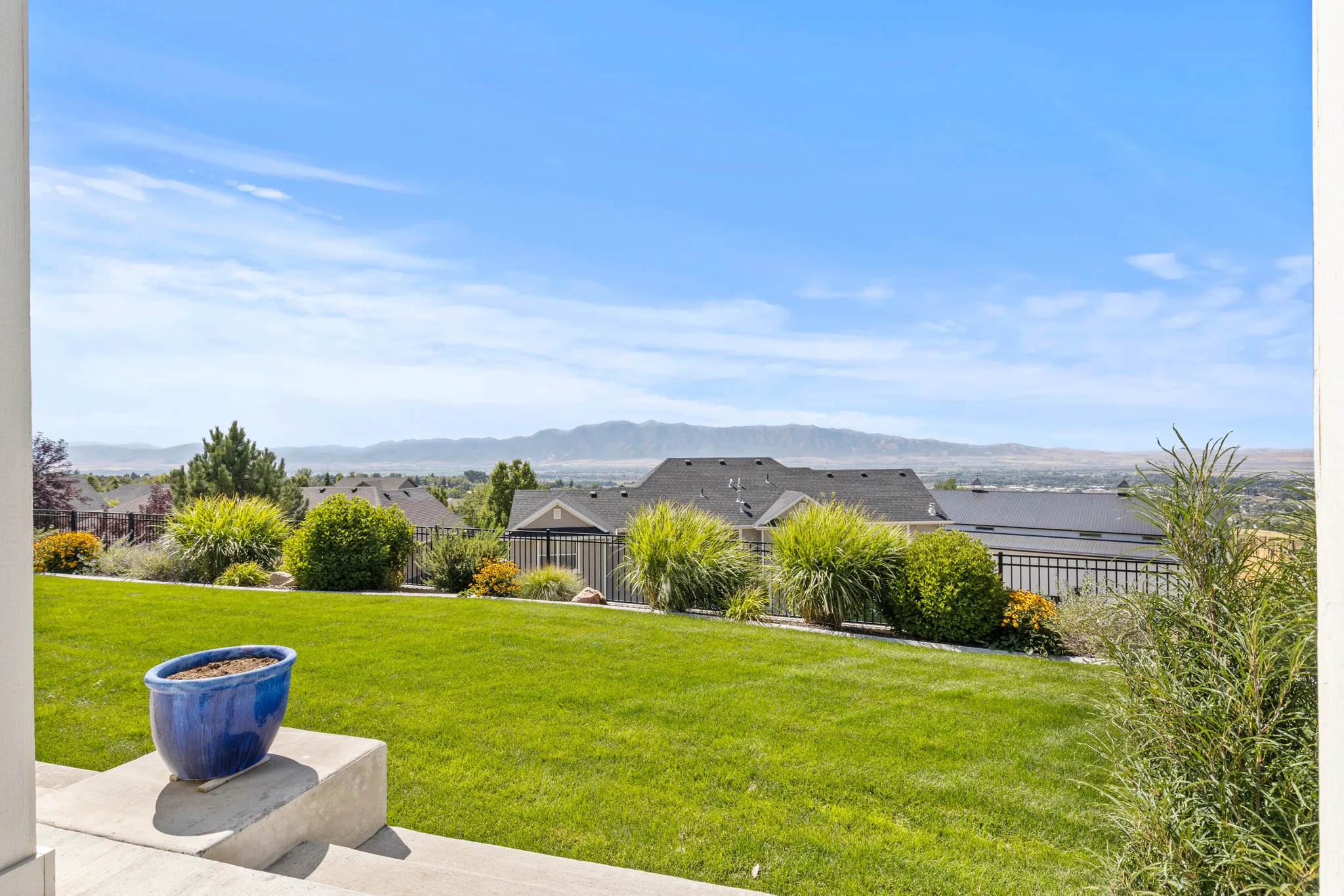 Expansive rear yard featuring a manicured lawn, established shrubbery, and a black wrought iron fence