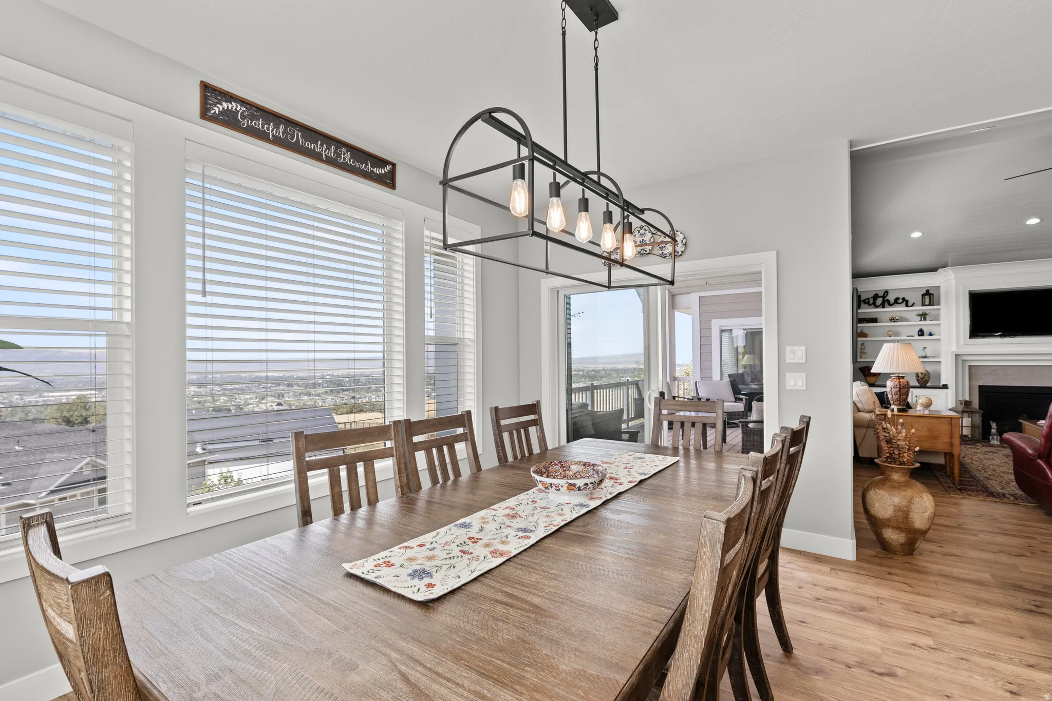Spacious dining area featuring a linear chandelier with exposed bulbs, three large windows, and light wood-finish flooring