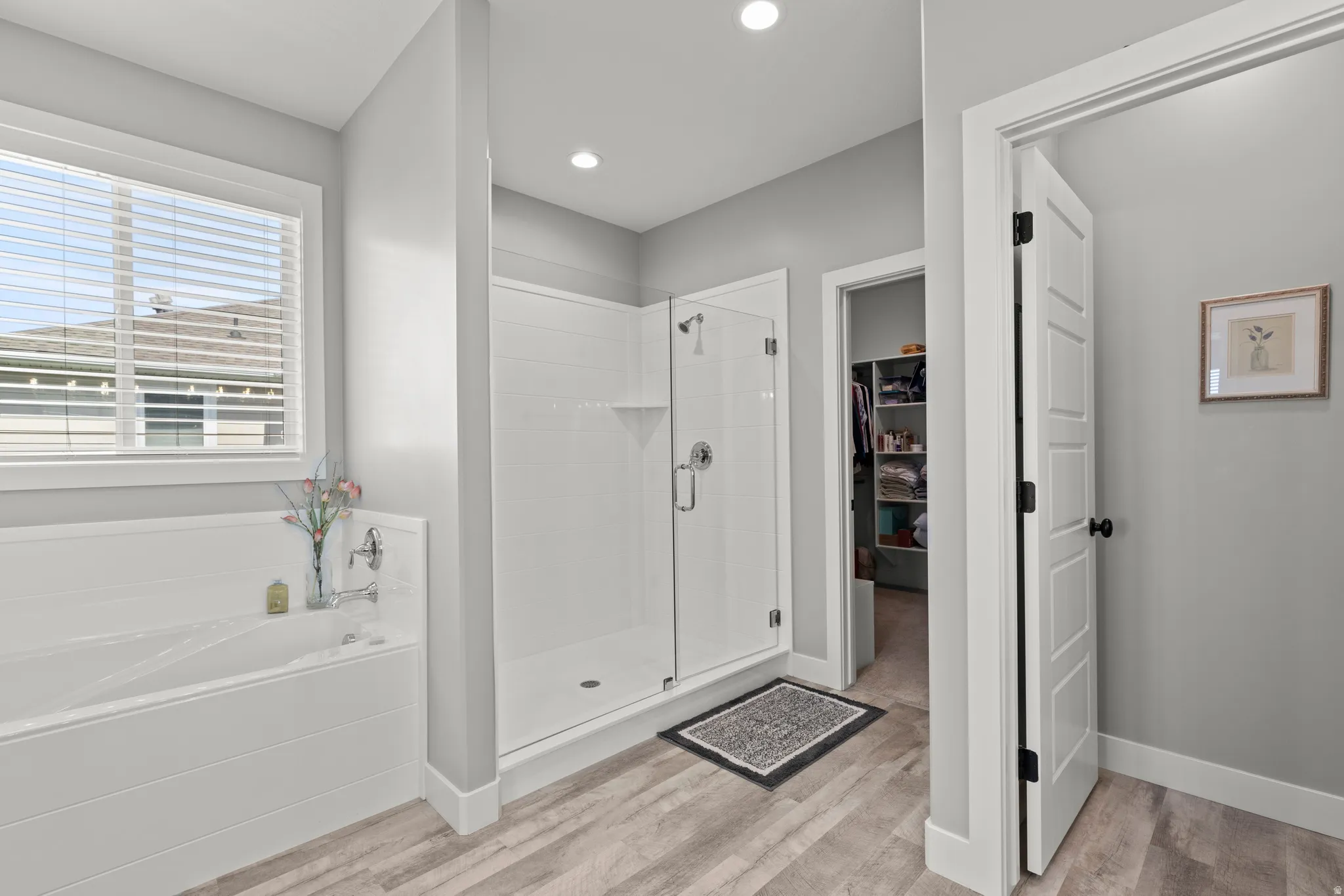 Bright bathroom featuring a large soaking tub with shiplap-style paneling, a glass-enclosed shower with subway tile, wood-finish flooring, and recessed lighting