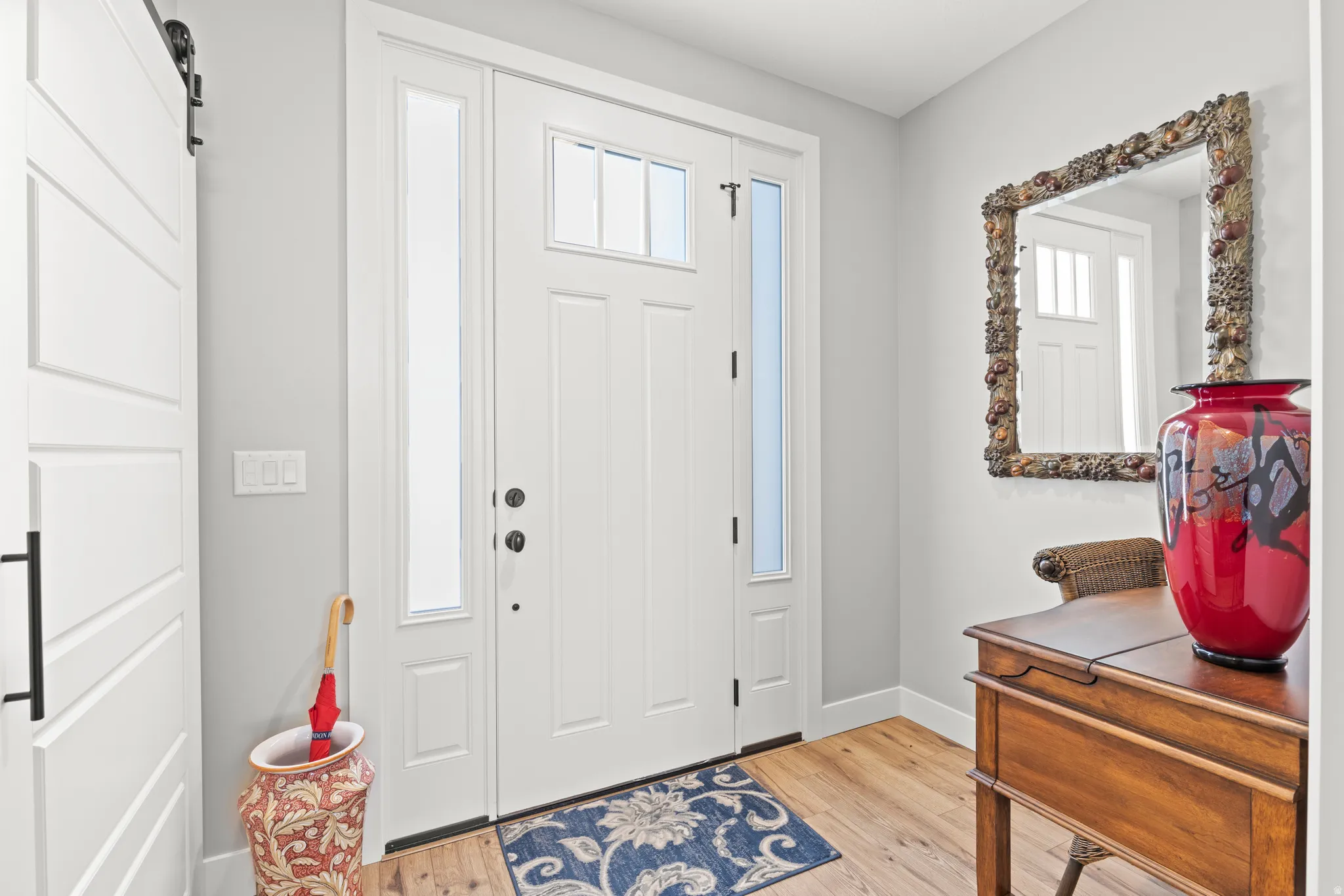 Entryway featuring a paneled door with transom and sidelight windows, light wood-finish flooring, and a white barn door with black hardware
