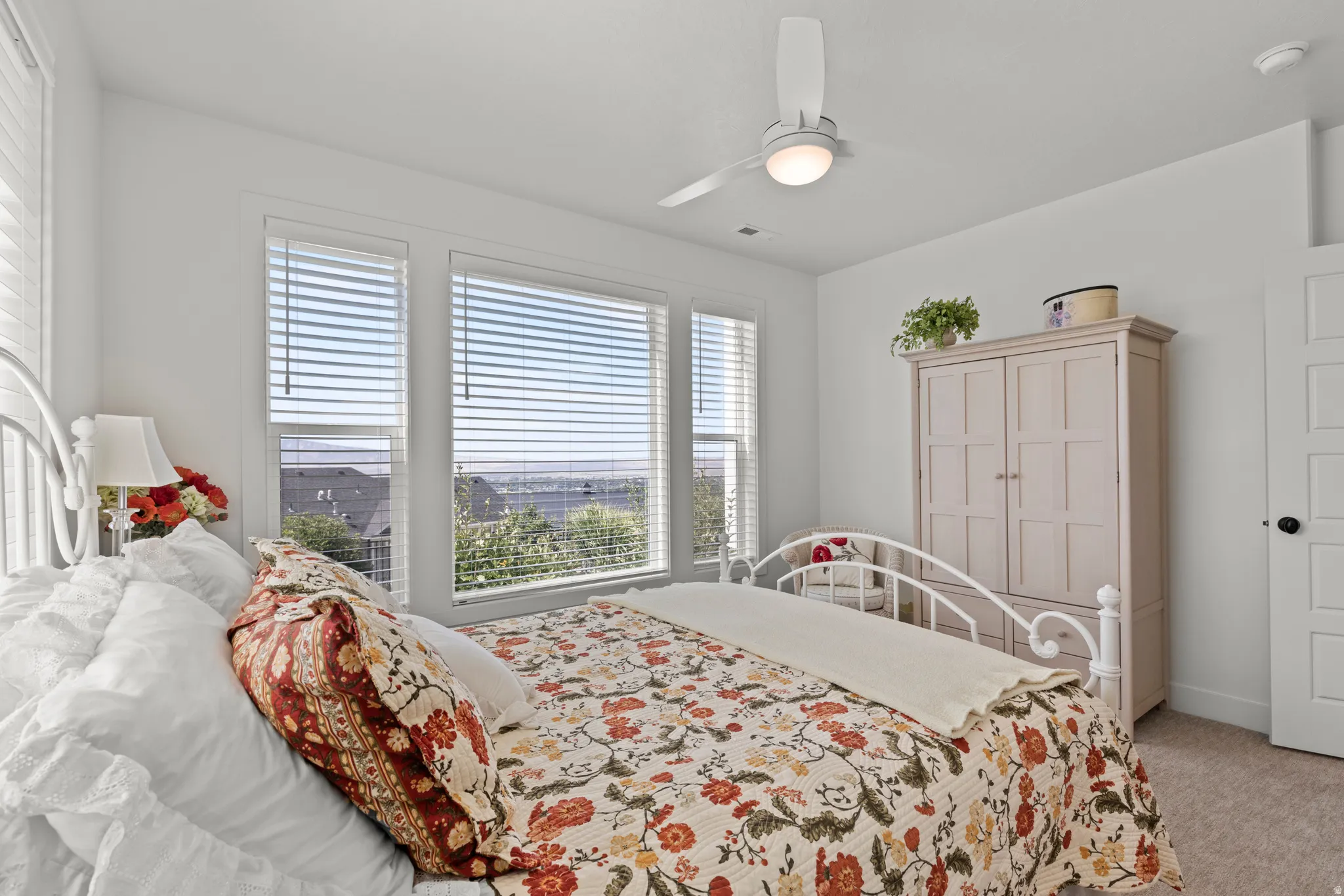 Bright room with multiple windows featuring blinds, a ceiling fan with integrated lighting, and neutral carpeting