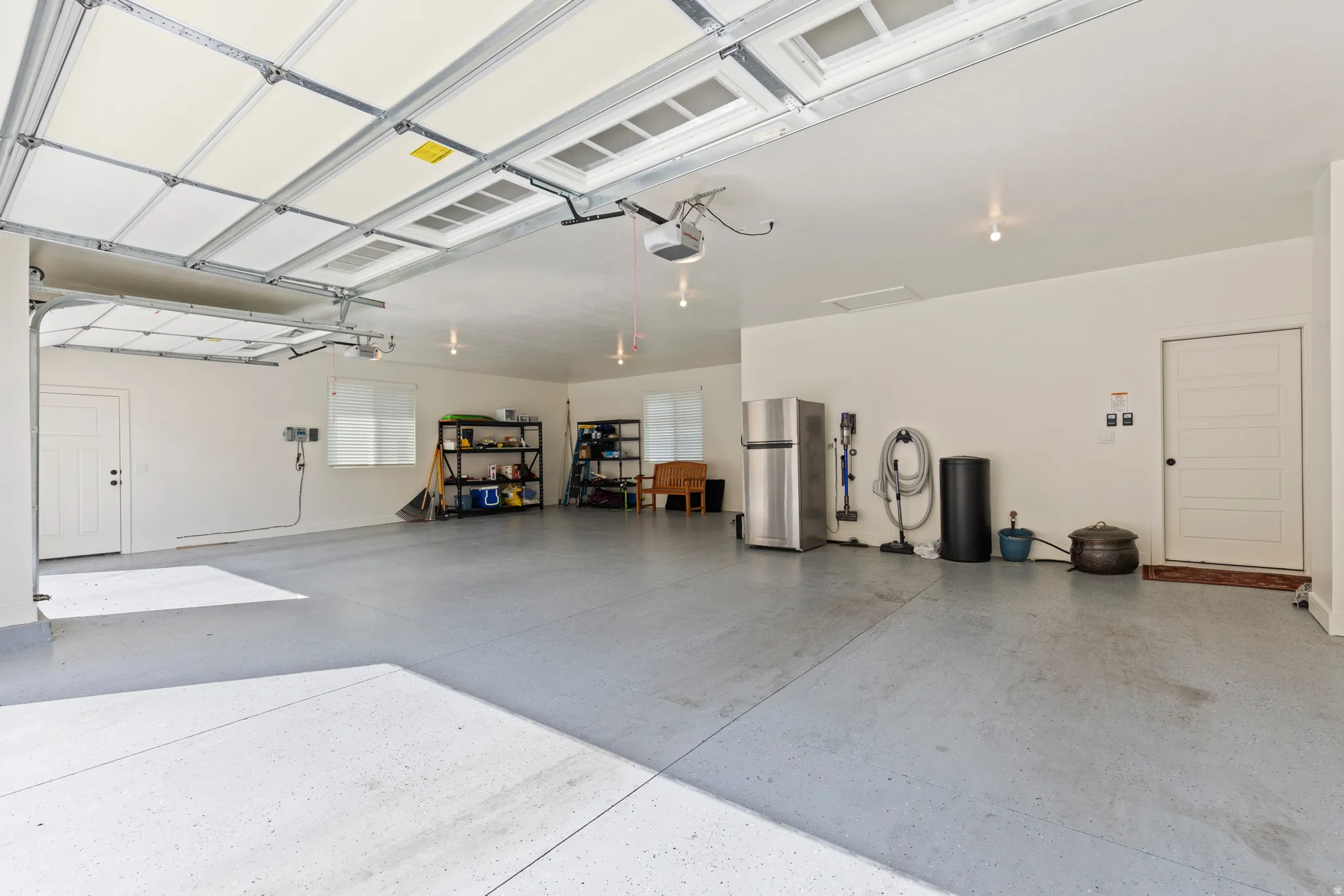 Spacious garage featuring a durable concrete floor with a light gray finish, overhead lighting, two white panel doors, and a window for natural light