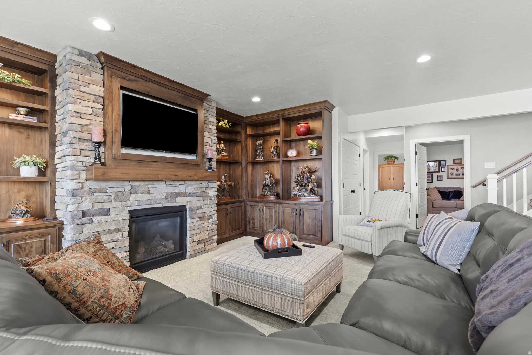 Living area featuring a stone-clad fireplace with an integrated television niche, custom wood-finish built-in shelving, and recessed lighting