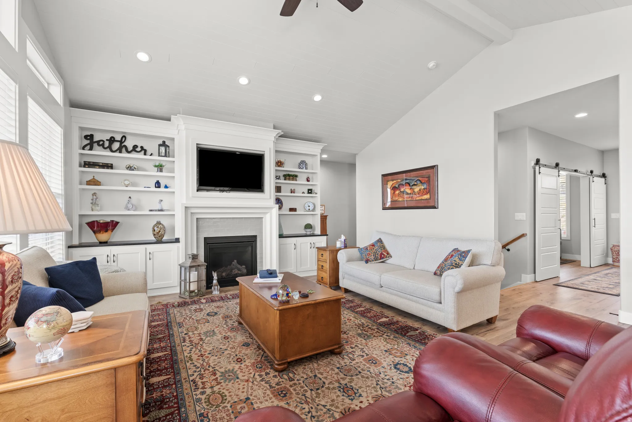Living area featuring vaulted ceilings with exposed beams, built-in shelving, a fireplace with a stone surround, and wood-finish flooring