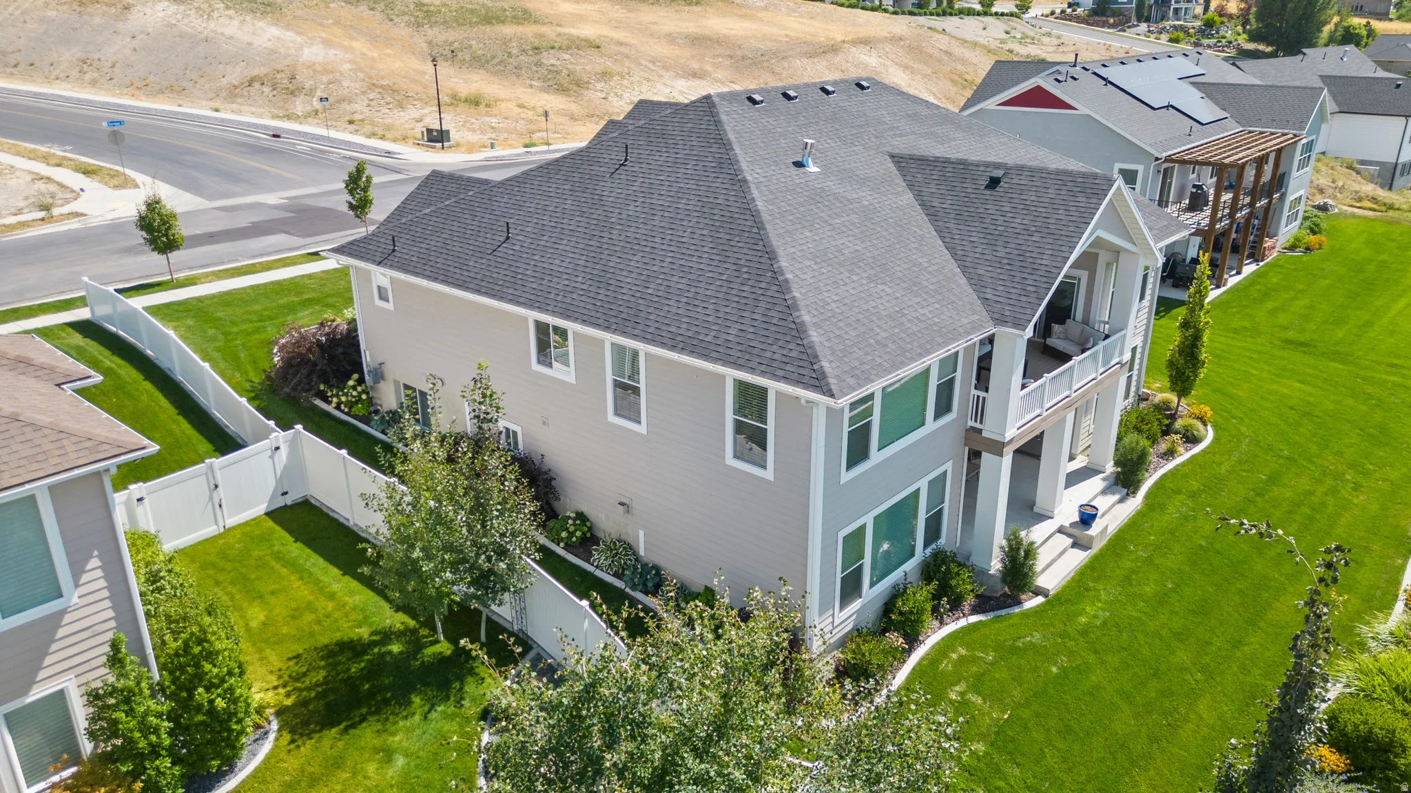 Two-story property featuring light grey siding, a dark shingle roof, and a white fence enclosing a manicured lawn