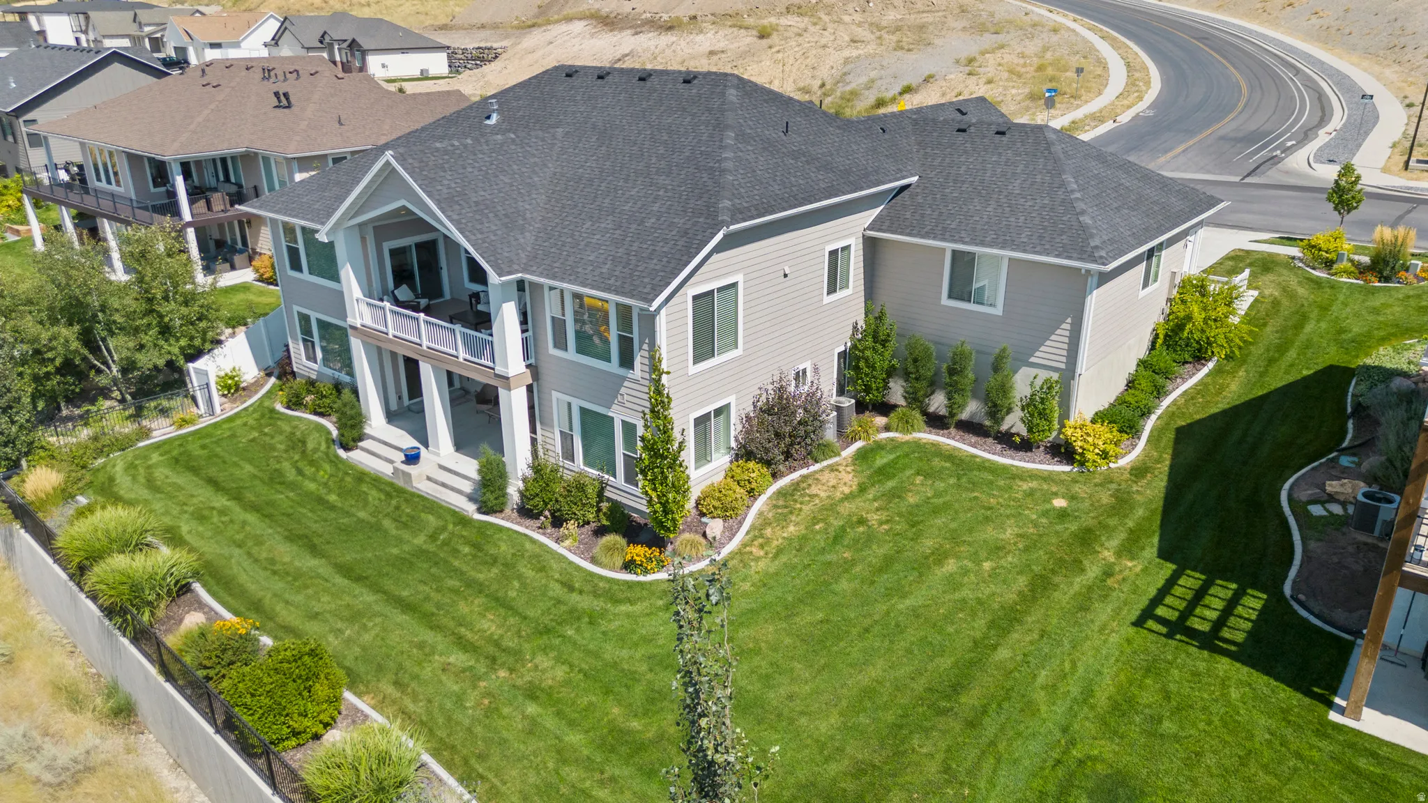 Contemporary residence featuring a two-story design with a balcony, an extended lower patio, and a spacious green lawn