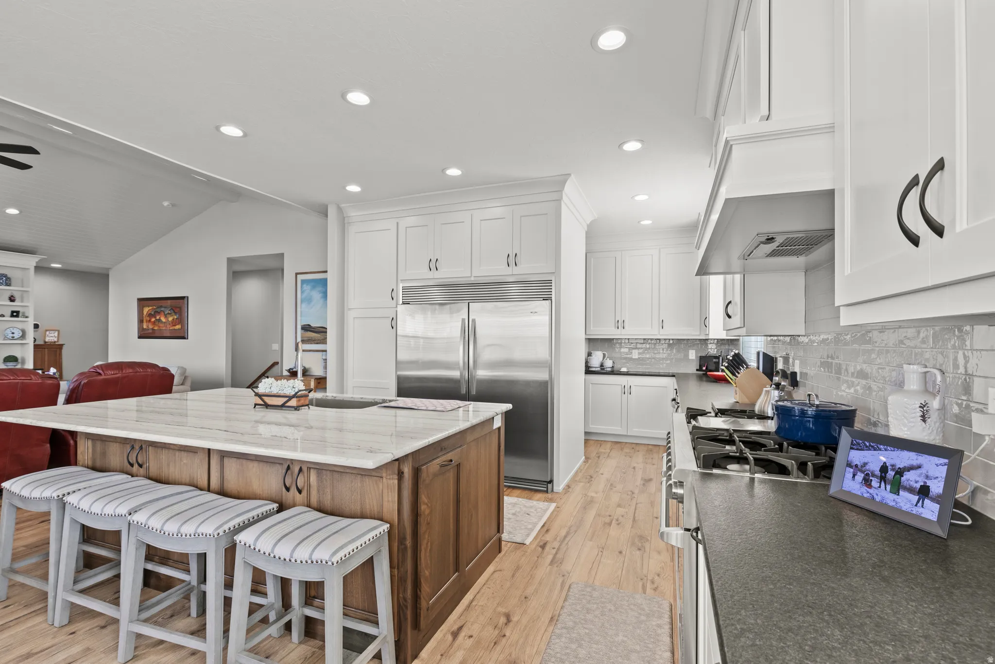 Spacious kitchen featuring a large central island with seating, stainless steel appliances, white shaker cabinetry, wood-finish flooring, and a subway tile backsplash