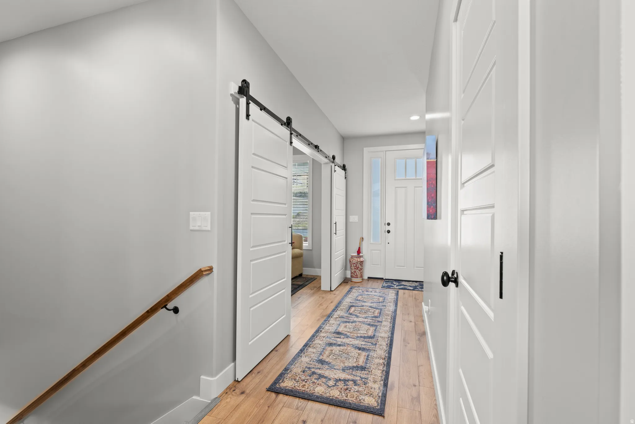 Foyer featuring wood-finish flooring, white paneled doors with black hardware, and a white front door with sidelights and transom window
