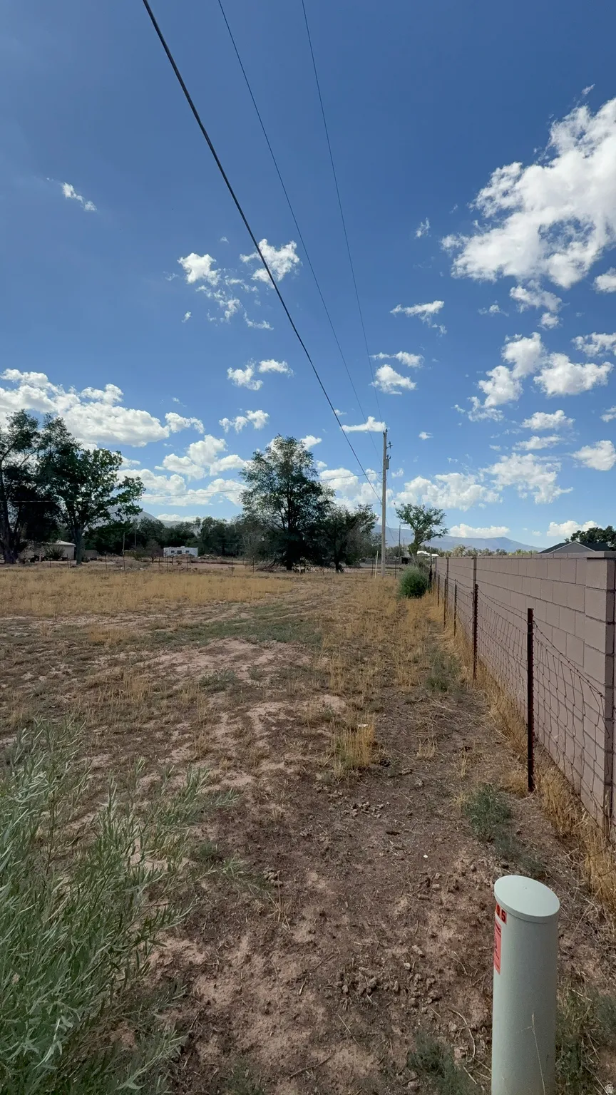 Expansive undeveloped lot with a partial block fence, mature trees in the background, and utility lines present