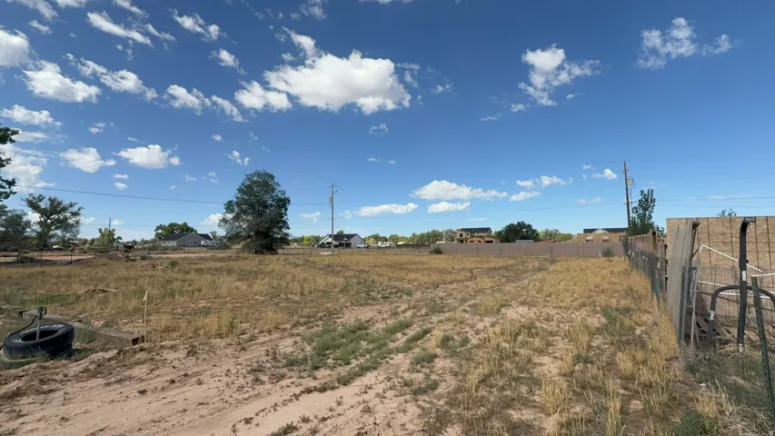 Expansive undeveloped lot featuring a chain-link fence, mature trees, and a dirt road bordering the property