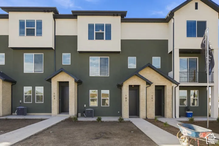 Multi-story townhome exterior featuring a mixed-material facade of stucco and stone veneer, multiple gabled entryways, and a private second-story balcony with metal railings