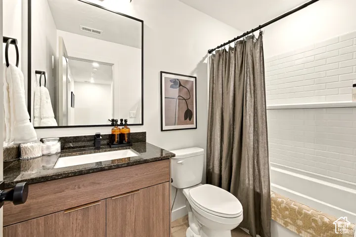 Bathroom featuring a wood-finish vanity, dark stone countertop with integrated sink, matte black hardware, square-edged mirror, and a tub-shower combination with white subway-style wall tiling