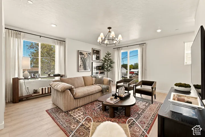 Living area featuring light-toned wood-finish flooring, multi-light chandelier, recessed lighting, and large windows with integrated blinds