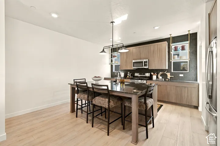 Kitchen featuring flat-panel wood-finish cabinetry, an expansive center island with a dark stone countertop, recessed lighting, and a textured black tile backsplash