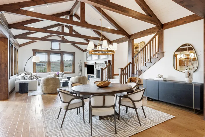 Spacious living area featuring exposed wood beams, vaulted ceilings, wood-finish flooring, a stone fireplace, and a prominent staircase with wood railings