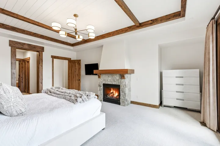 Spacious room featuring a stone fireplace with a wood mantle, a white shiplap ceiling with exposed wood beams, and a contemporary light fixture
