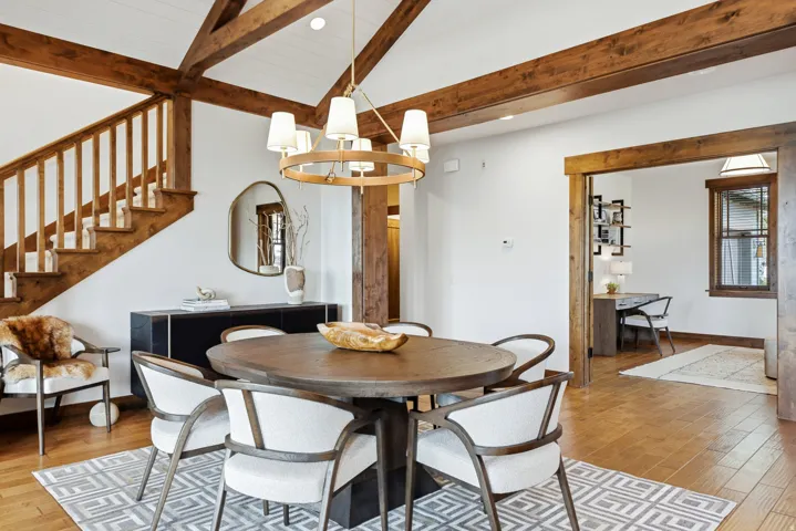 Dining area featuring a contemporary chandelier, exposed wood ceiling beams, wood-finish flooring, and a built-in staircase with wood railing