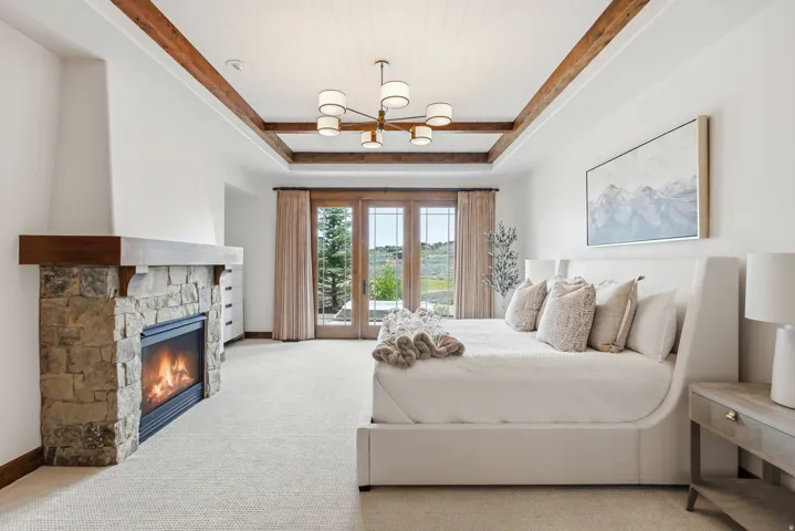 Spacious room featuring a stone-clad fireplace with wood mantel, a wood-beamed tray ceiling with beadboard detail, and a contemporary chandelier