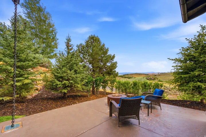 Stamped concrete patio featuring a built-in fire pit, surrounded by mature evergreen trees and natural landscaping