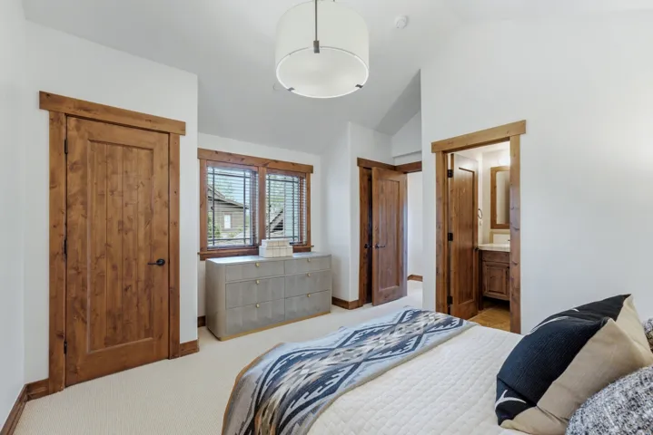 Vaulted ceiling room with wood-finish doors and trim, neutral carpeting, and a modern drum pendant light fixture