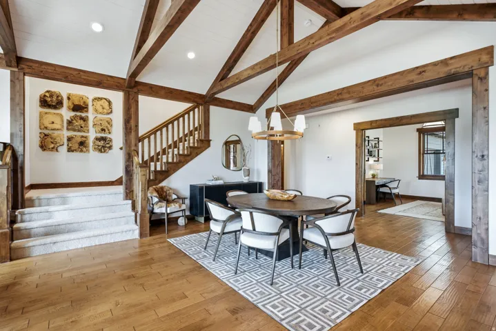 Vaulted ceiling with exposed wood beams, hardwood flooring, and a carpeted staircase with wood railing