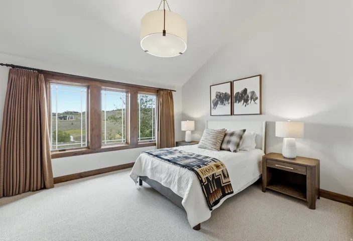 Bedroom featuring three large windows with dark wood frames, vaulted ceilings, and light-colored carpeting