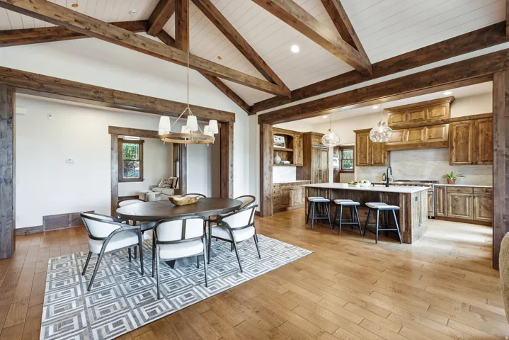 Spacious open-concept living area featuring a vaulted ceiling with exposed wood beams, light wood-finish flooring, and recessed lighting