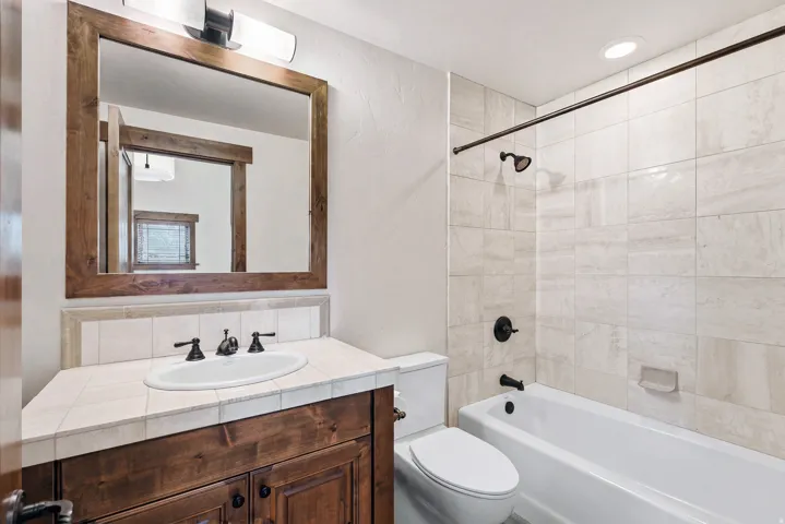 Bathroom featuring a wood-finish vanity with a tile countertop, an undermount sink, and dark bronze fixtures