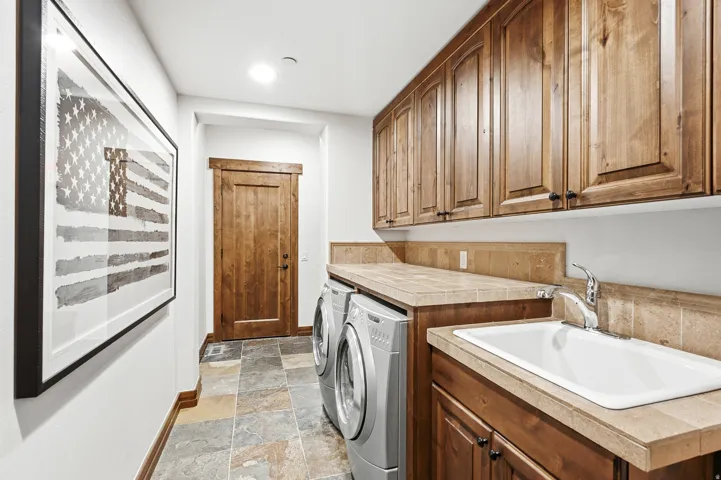 Laundry room featuring wood cabinetry, stone tile flooring, a utility sink, and a solid-surface countertop