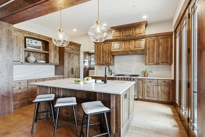Gourmet kitchen featuring a substantial central island with seating, custom wood cabinetry, stainless steel range with integrated hood, light-toned backsplash, and French doors