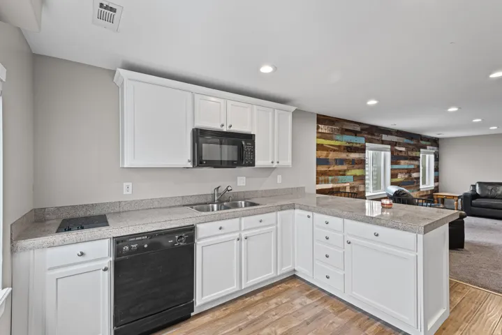Modern kitchenette featuring white cabinetry, a double basin stainless steel sink, built-in appliances, and light-toned countertops