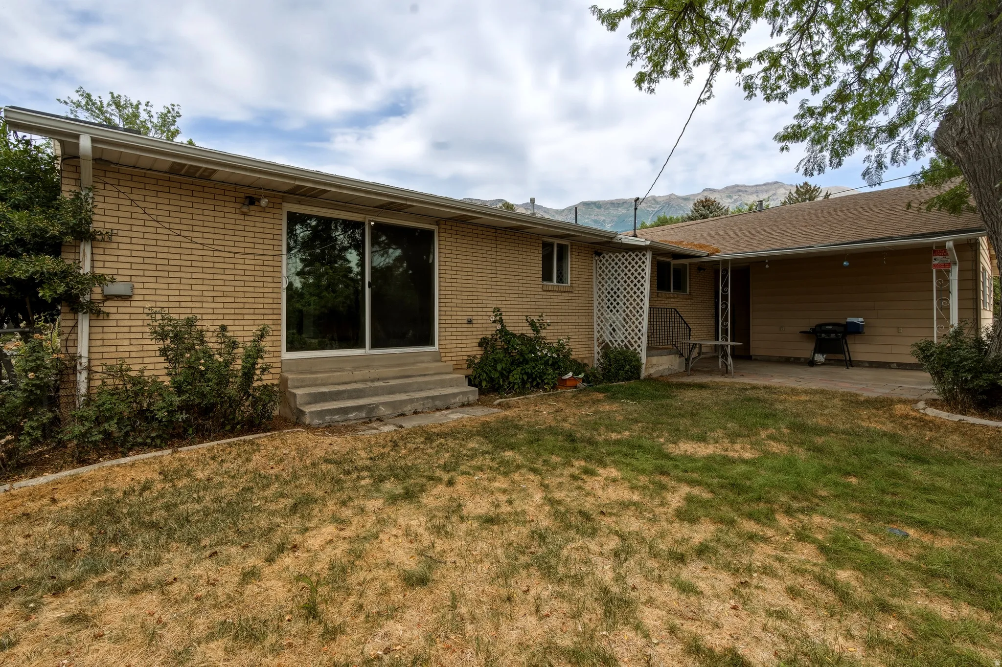 Rear exterior featuring brick siding, sliding glass door, concrete steps, a covered patio area, and a mountain backdrop