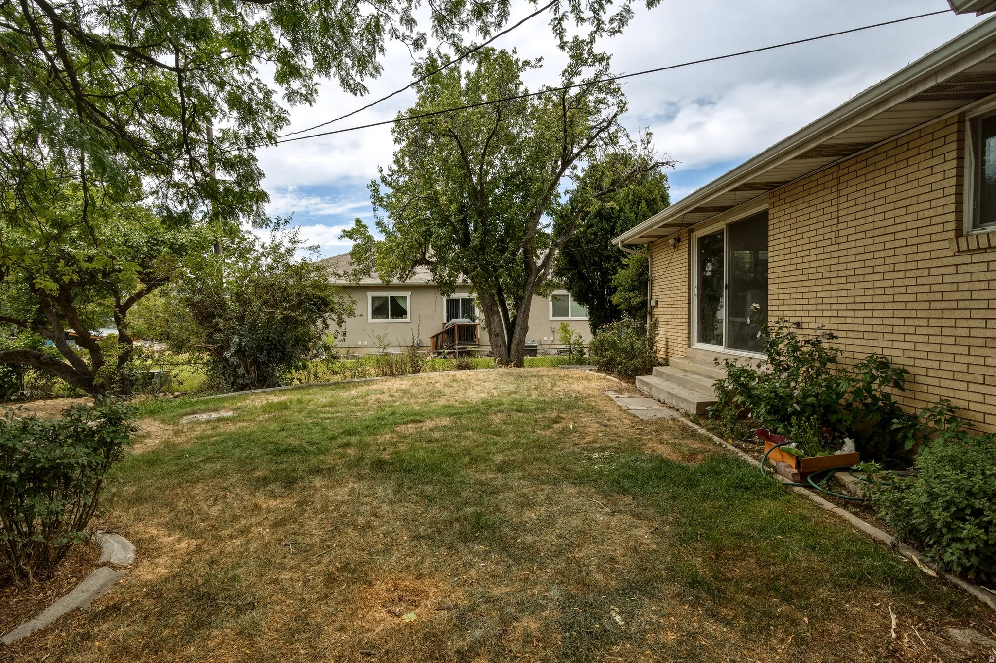 Expansive exterior featuring mature trees, a gently sloped lawn, and a brick-sided structure with a sliding glass door